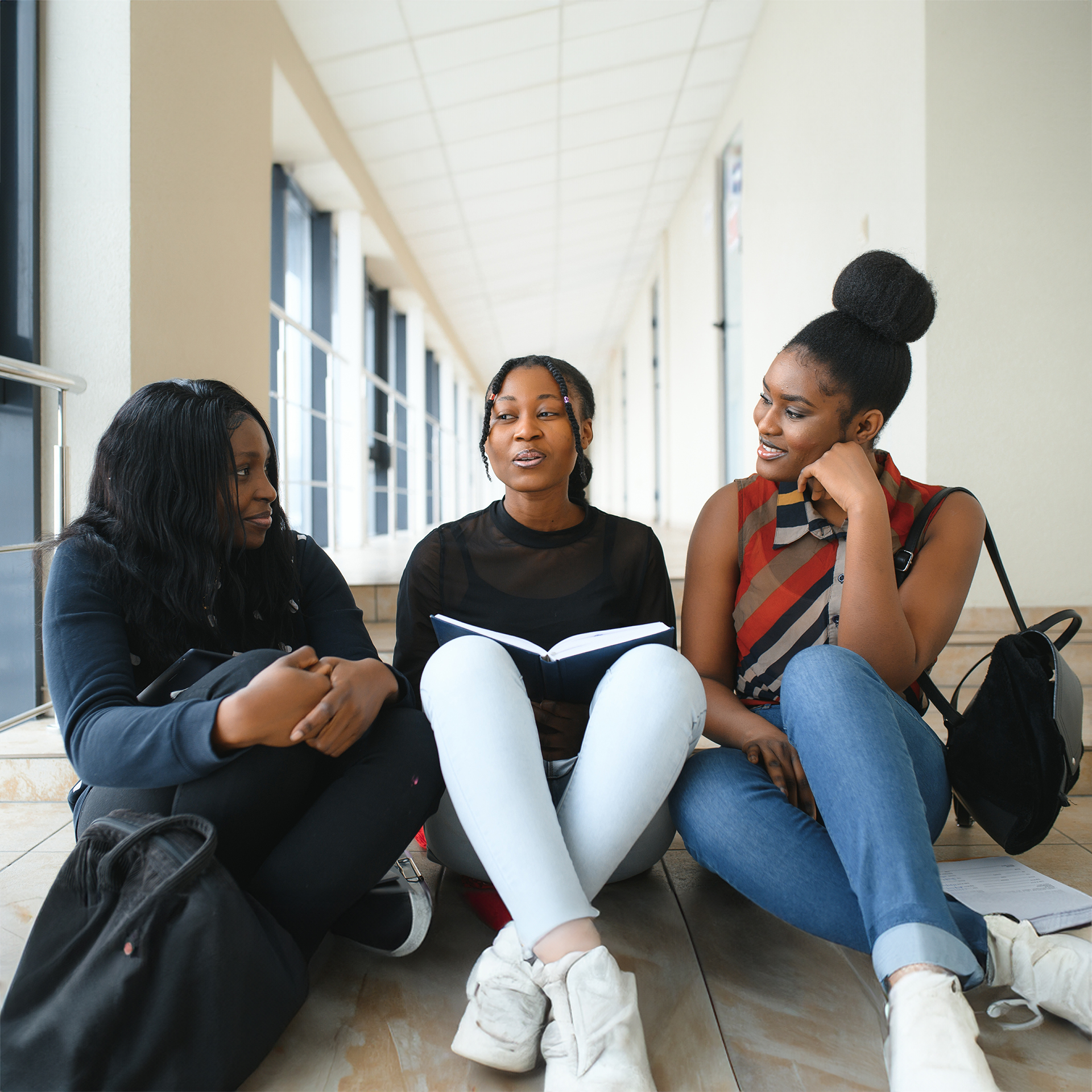 Two hipster girls discussing route of future travel sitting outdoors in urban setting Three girls discussing in hallway
