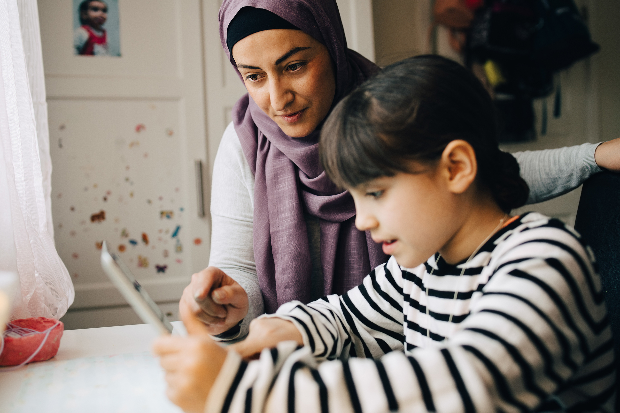 Mature mother assisting girl in homework while using digital tablet at home